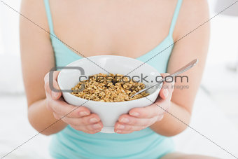 Mid section of a female with a bowl of cereal sitting on bed