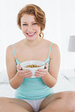 Smiling female with a bowl of cereal sitting on bed