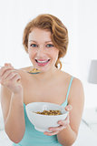 Smiling young female with a bowl of cereal sitting on bed