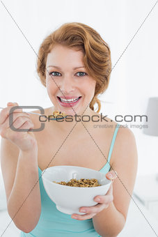 Smiling young female with a bowl of cereal sitting on bed