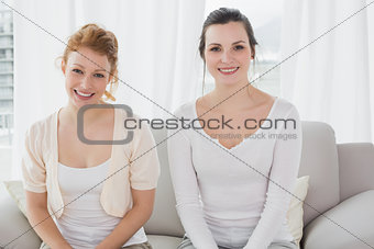 Two smiling young female friends sitting on sofa