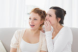 Female friends gossiping as they look away in living room