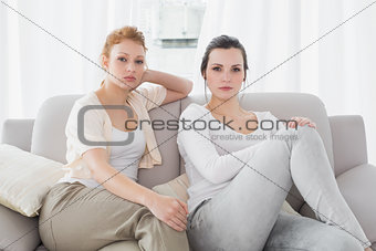Two serious female friends sitting on sofa in the living room