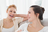 Two cheerful female friends sitting on sofa in living room