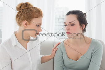 Young woman consoling female friend sitting on sofa