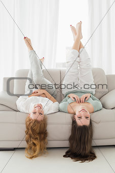 Female friends lying on sofa with legs in the air in living room