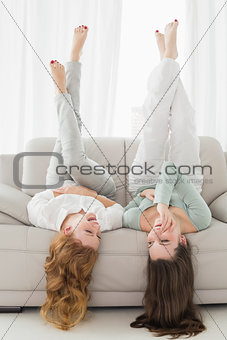 Female friends lying on sofa with legs in the air in living room