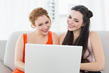 Female friends using laptop together at home
