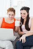 Female friends using laptop together at home