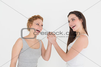 Two cheerful young female friends arm wrestling