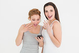Shocked casual female friends with mobile phone