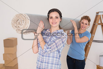 Female friends carrying rolled rug after moving in a house