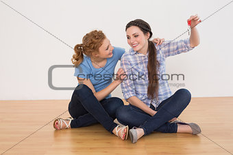 Female friends with house keys sitting on the floor