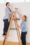 Friends with paintbrush and can on ladder in a new house