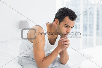 Thoughtful young man sitting on bed