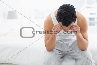 Young sleepy man rubbing his eyes on bed