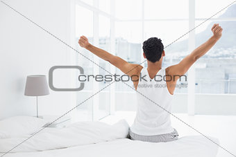 Rear view of a man stretching arms in bed
