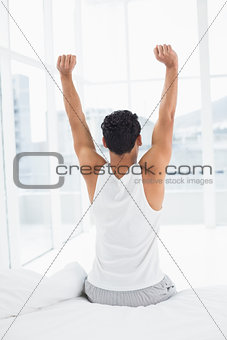 Rear view of a man stretching arms in bed