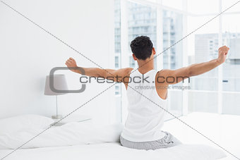 Rear view of a young man stretching arms in bed