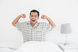 Smiling man stretching his arms in bed