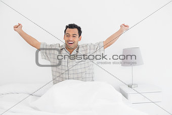 Smiling man stretching his arms in bed