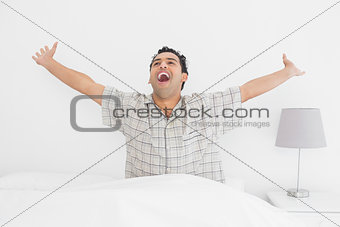 Smiling young man stretching his arms in bed