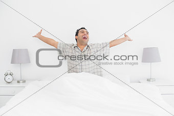 Cheerful man stretching his arms in bed