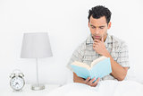 Serious relaxed man reading book in bed