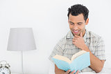 Smiling relaxed man reading book in bed