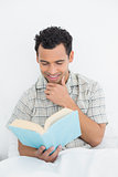 Smiling young man reading book in bed
