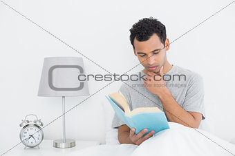 Relaxed young man reading book in bed
