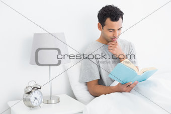Relaxed man reading book in bed