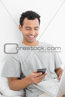 Casual smiling man with laptop text messaging in bed