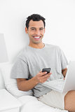 Casual smiling man with laptop text messaging in bed