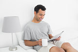 Relaxed man with newspaper and coffee cup in bed