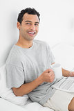 Relaxed man with newspaper and coffee cup sitting on bed