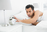 Man in bed extending hand to alarm clock