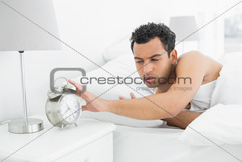Man in bed extending hand to alarm clock