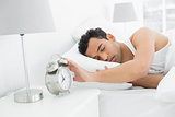 Sleepy man extending hand to alarm clock