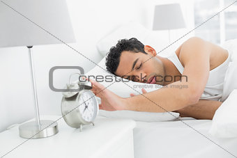 Sleepy man extending hand to alarm clock