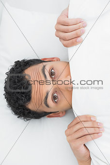 Shocked man covering face with sheet in bed