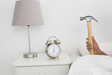 Hand smashing alarm clock with hammer in bed