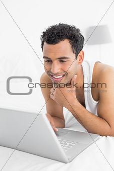 Smiling casual man using laptop in bed