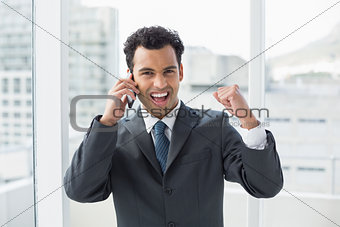 Cheerful elegant young businessman using cellphone in office