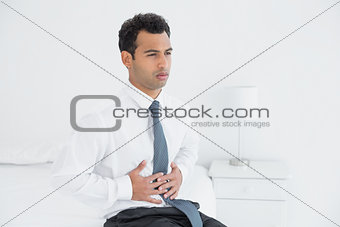 Businessman with stomach pain sitting on bed