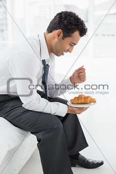 Businessman sitting on bed with a plate of croissants