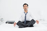 Relaxed businessman sitting in lotus pose on bed