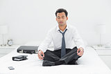 Relaxed young businessman sitting in lotus pose on bed