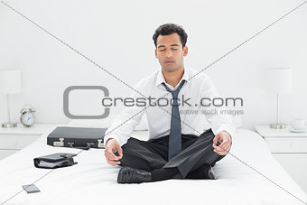 Relaxed young businessman sitting in lotus pose on bed