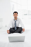 Businessman sitting in lotus pose with laptop on bed